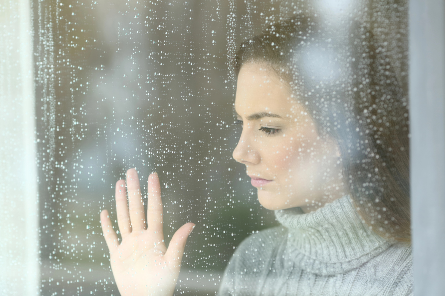 pondering woman looking through window at rain